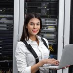 Woman in server room, operating laptop.